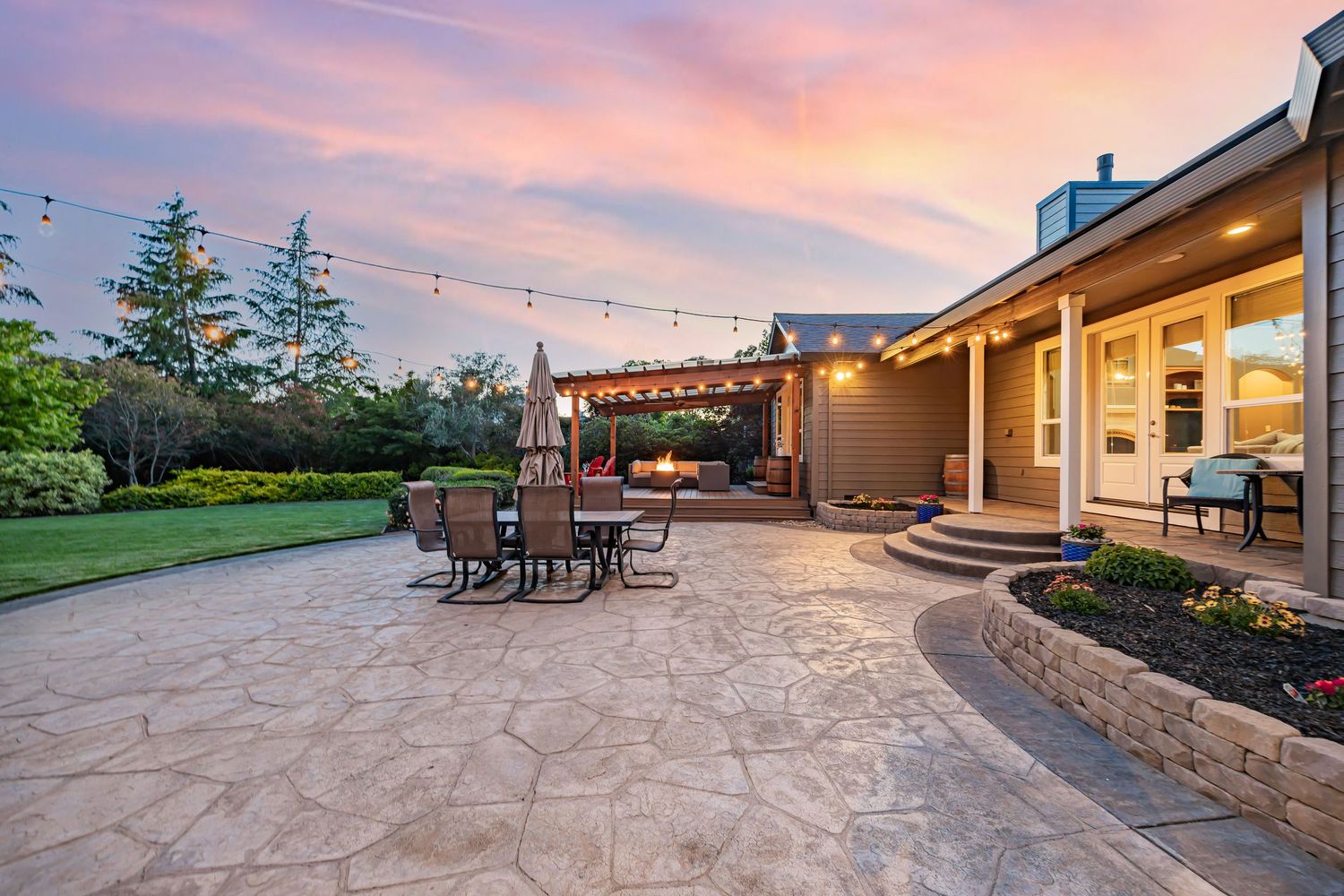 Expansive curved patio with dining area and string lights against pink evening sky.