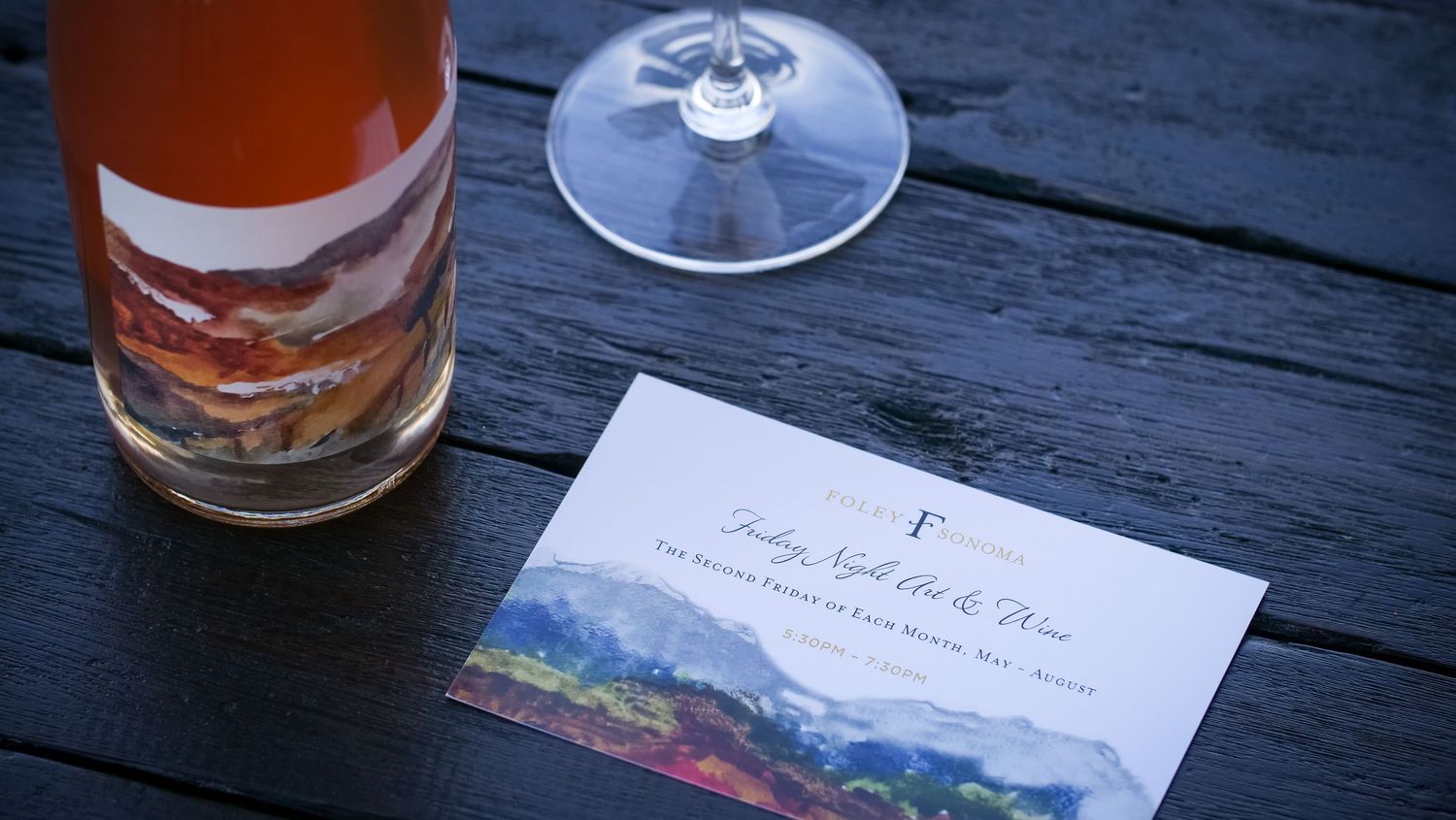Wine bottle and tasting menu card on rustic wooden table outdoors.