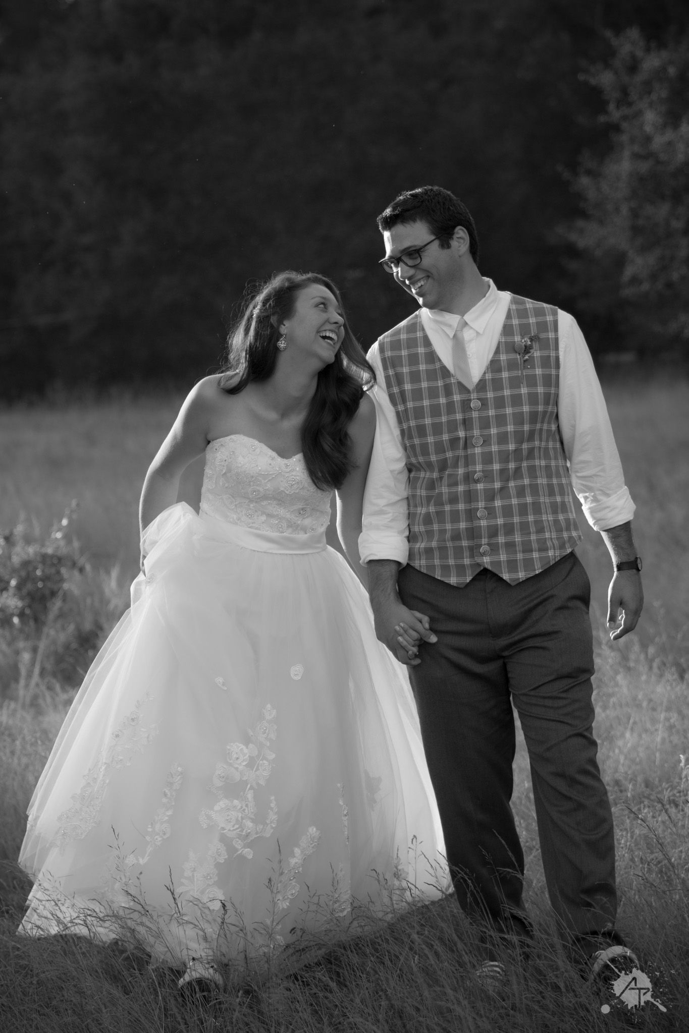 Black and white portrait of joyful couple walking through tall grass.