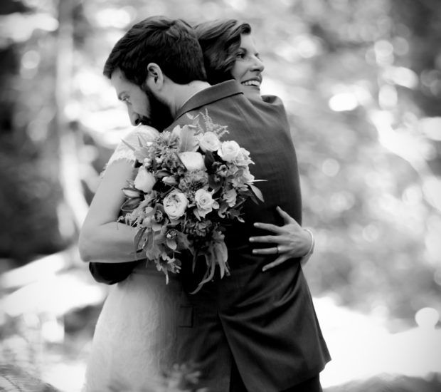 Black and white photo captures an intimate embrace during a forest wedding ceremony.