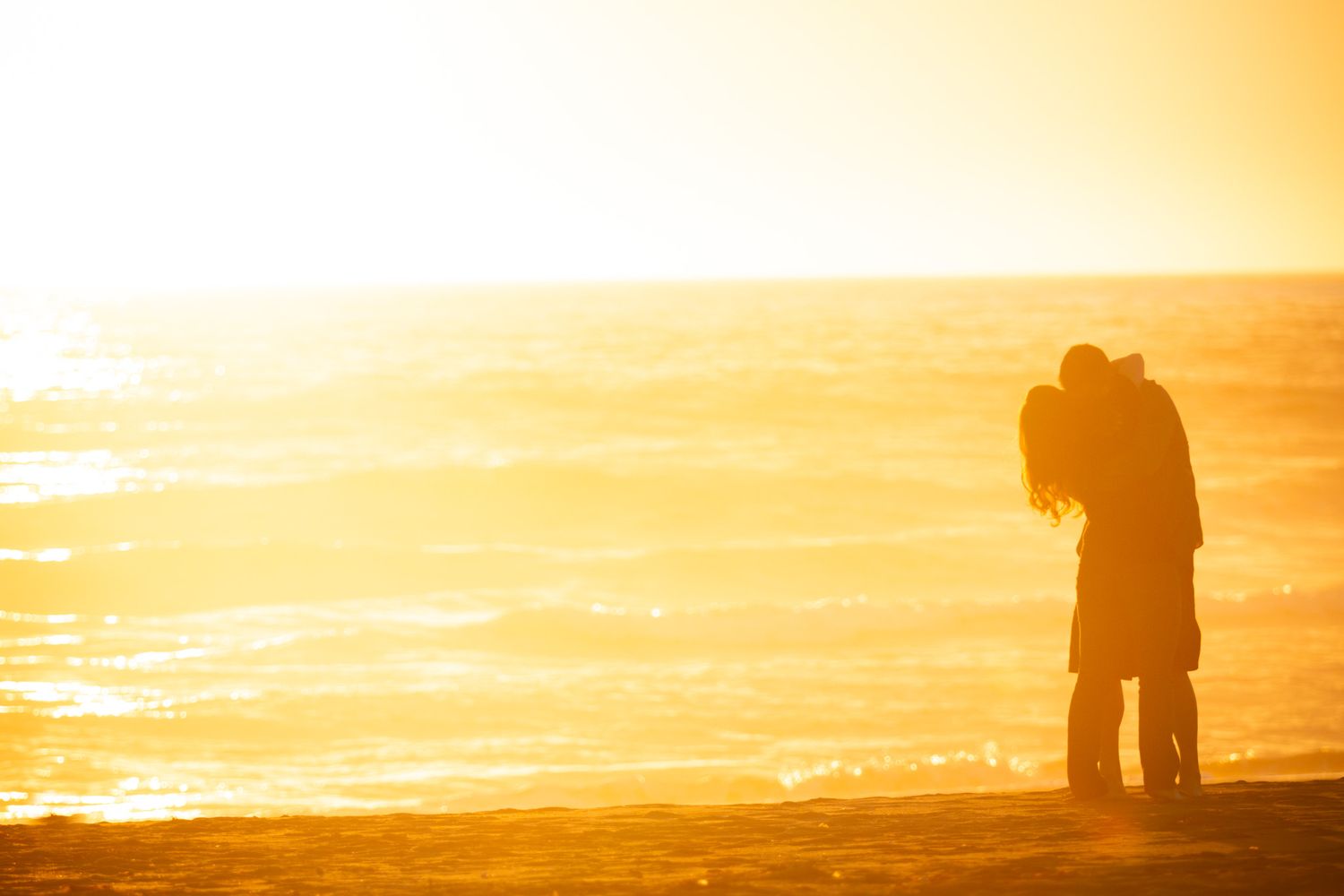 Two silhouettes embrace against a dramatic golden sunset on the beach.