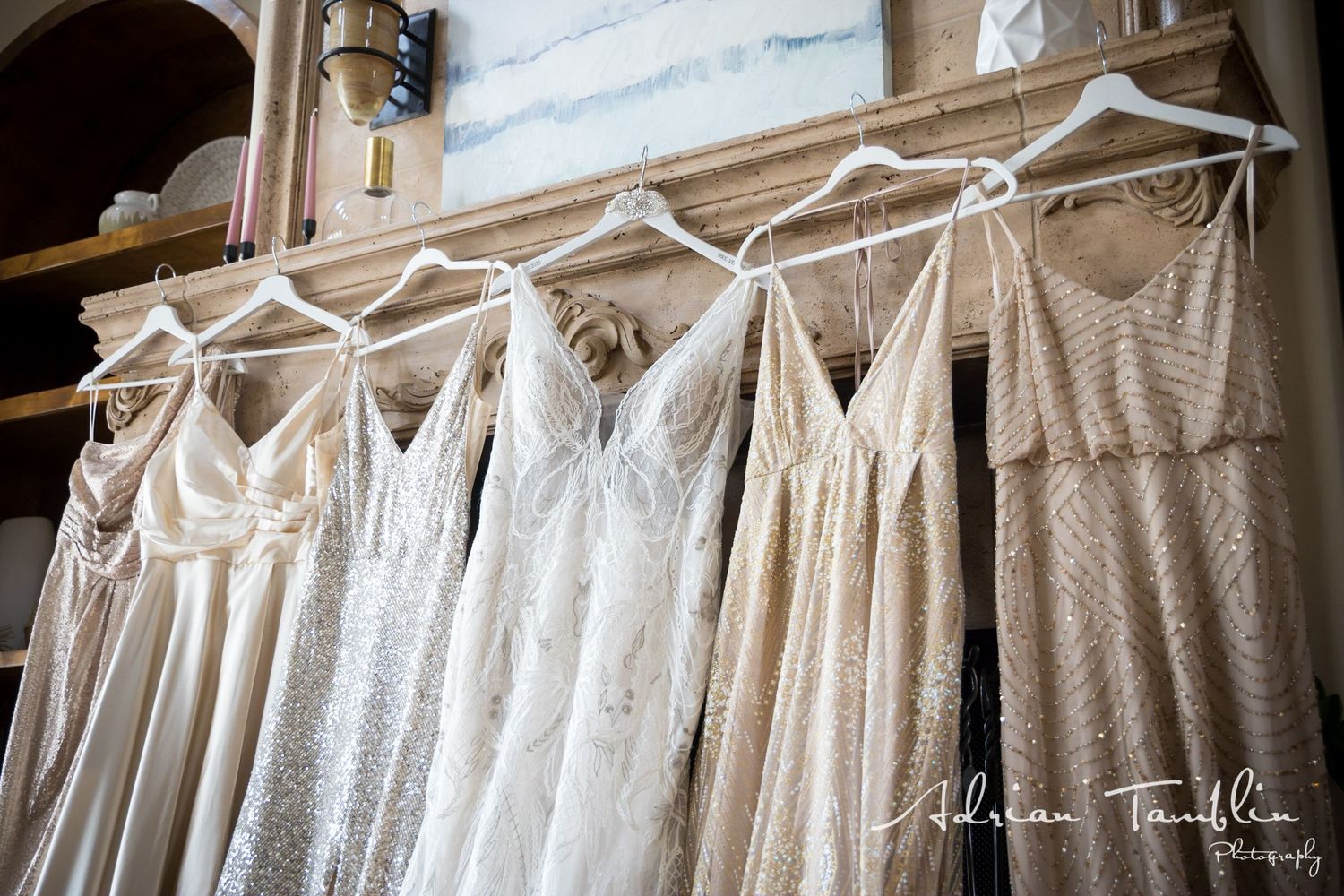 Row of light colored bridesmaid dresses hanging on wooden hangers.