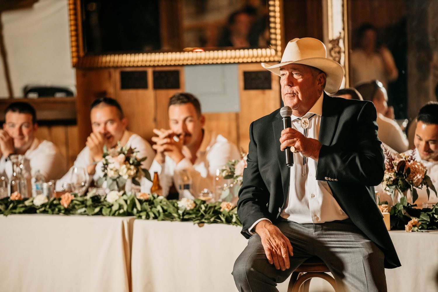 A speaker in a cowboy hat delivers a heartfelt toast at the wedding head table.