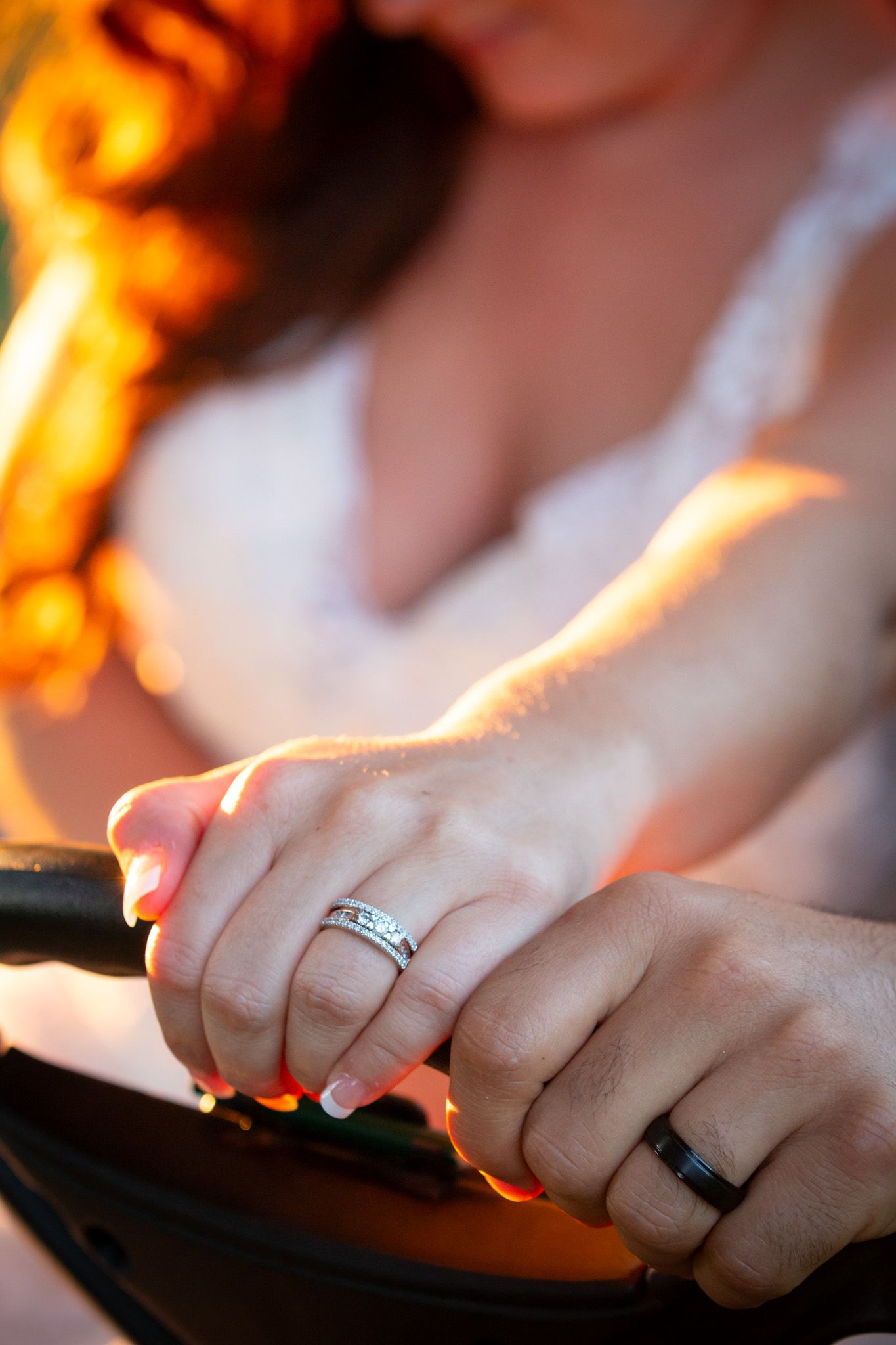 Close-up of wedding rings on hands in warm sunset lighting.