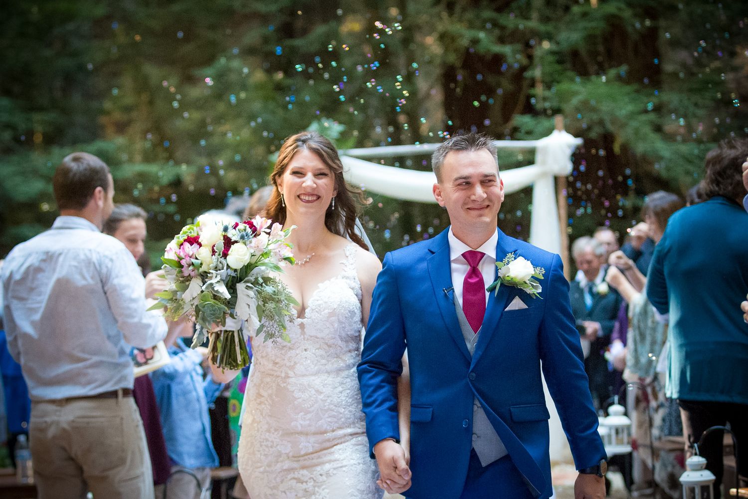 Newlyweds walk hand in hand through celebrating guests at their outdoor forest wedding.