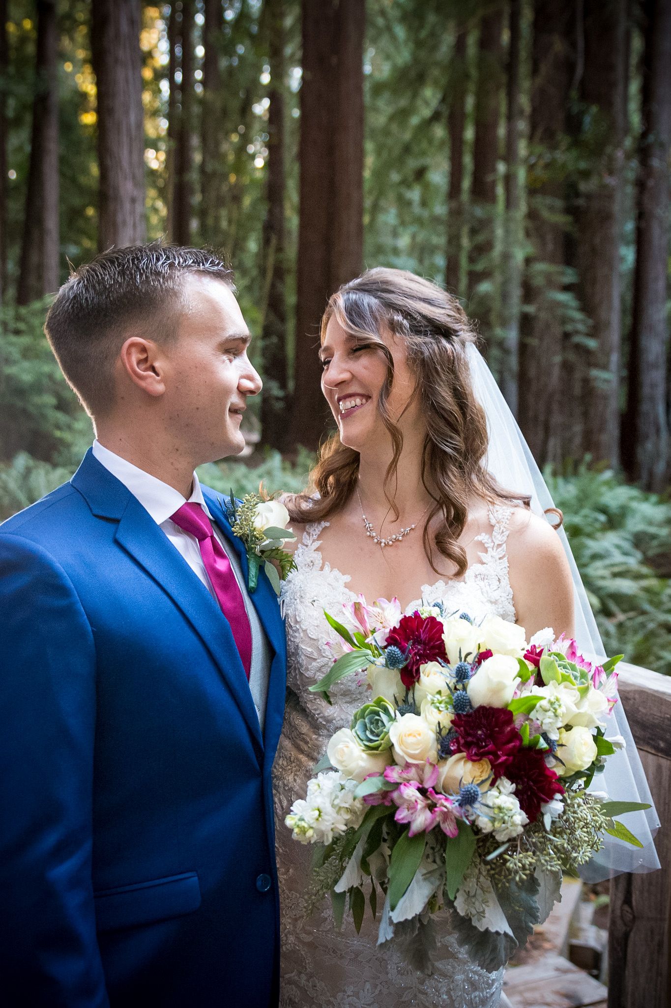 Romantic wedding portrait of couple in blue suit and lace gown surrounded by redwood forest scenery.