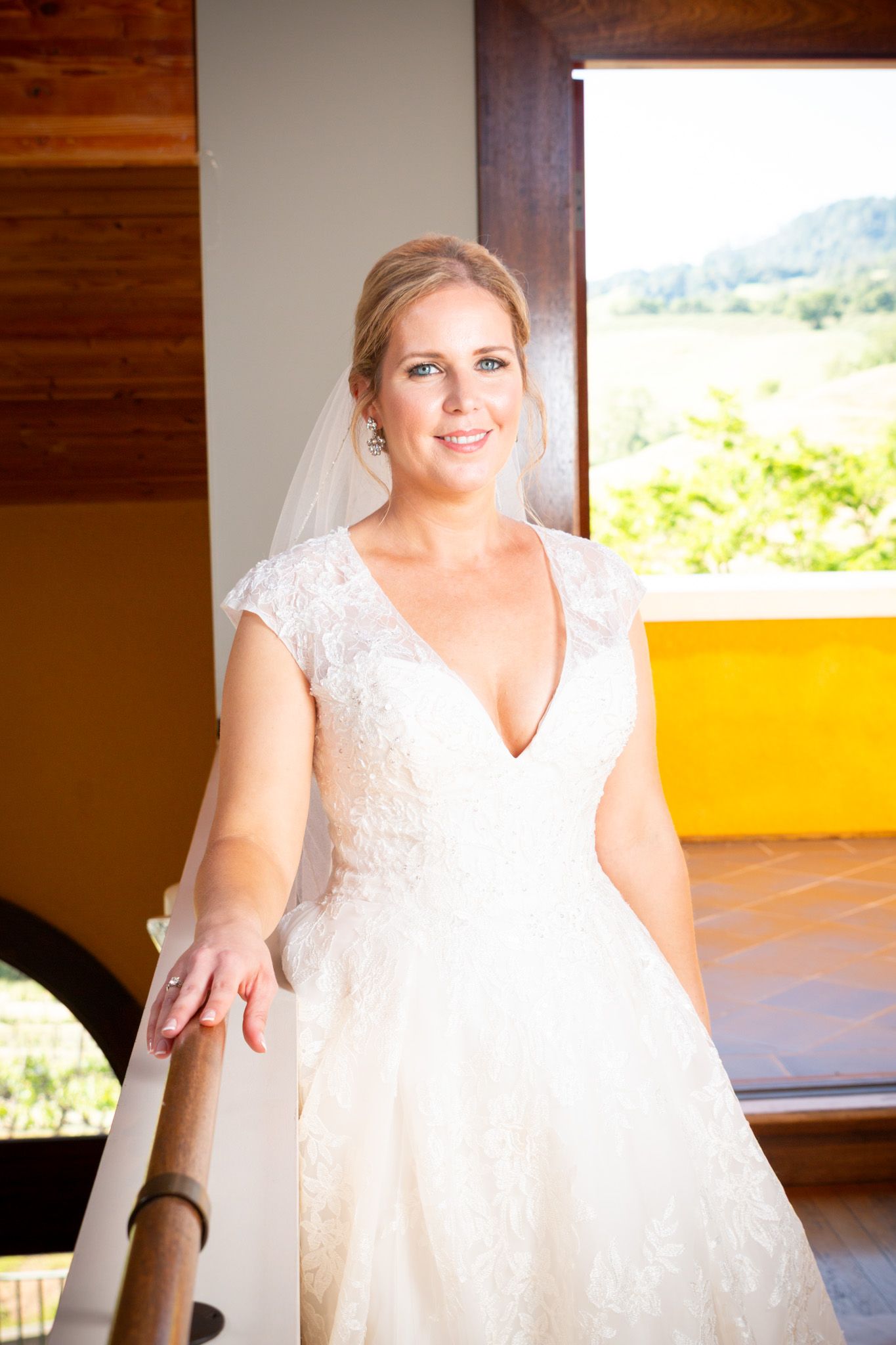 Bride in white v-neck lace dress poses by window with mountain view.