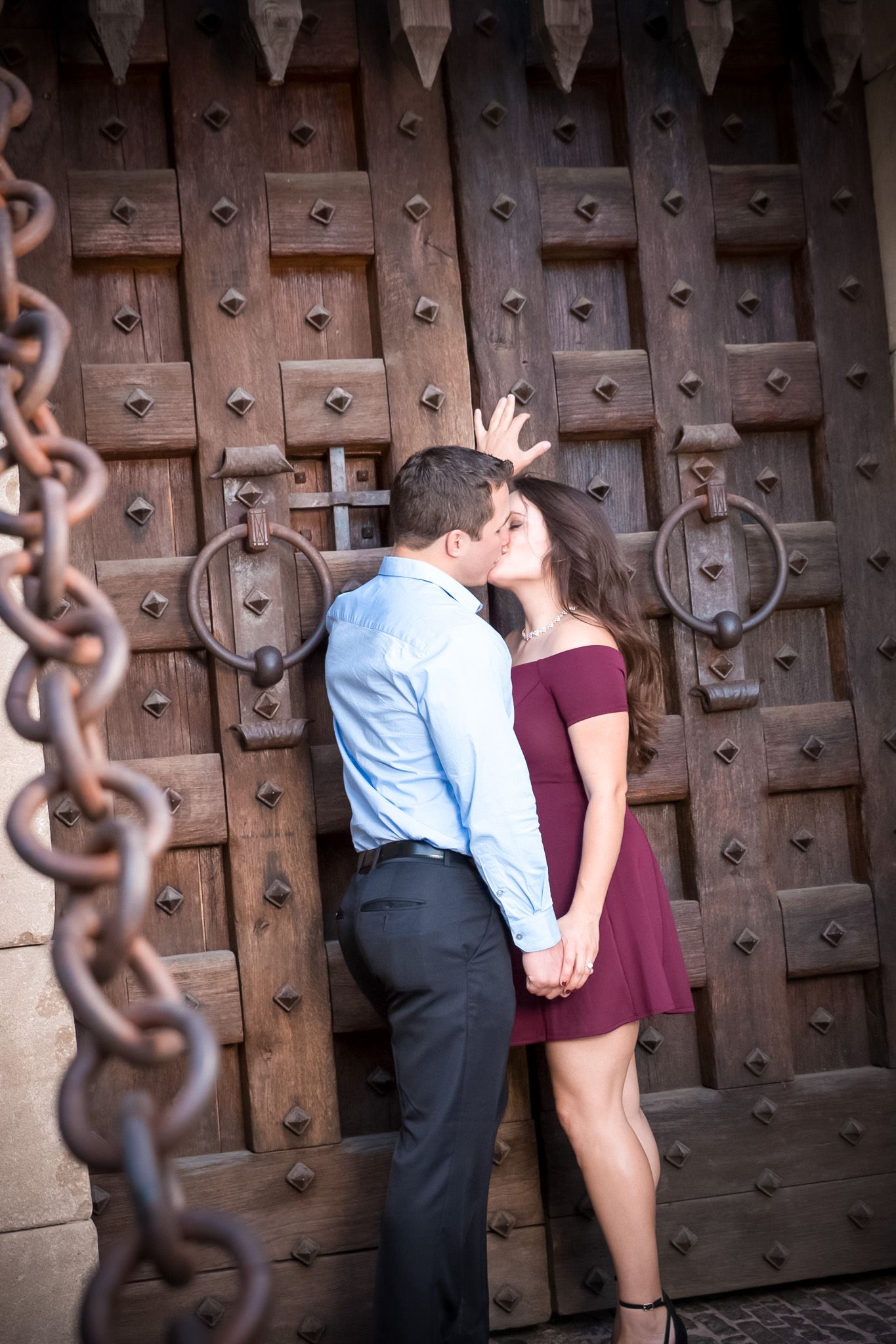 Intimate engagement photo against a decorative medieval door with chains.