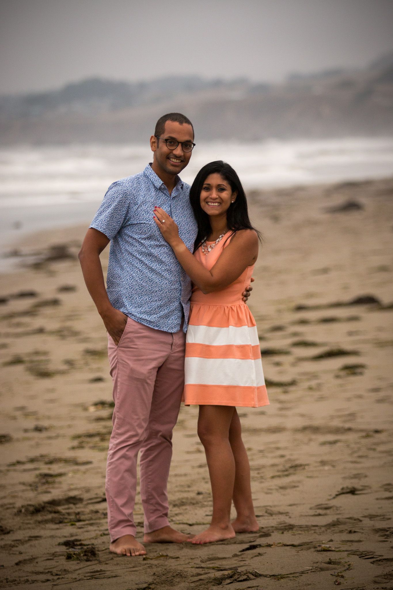 Couple posing together on beach at sunset wearing coordinated casual outfits.