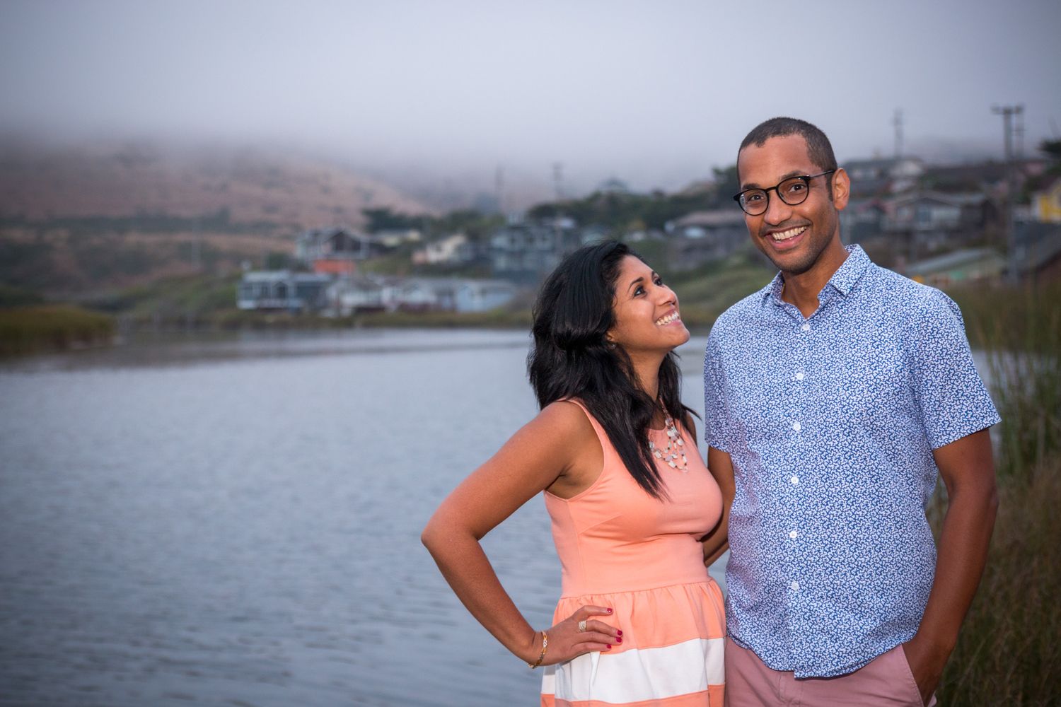 A couple posing by the water during sunset.