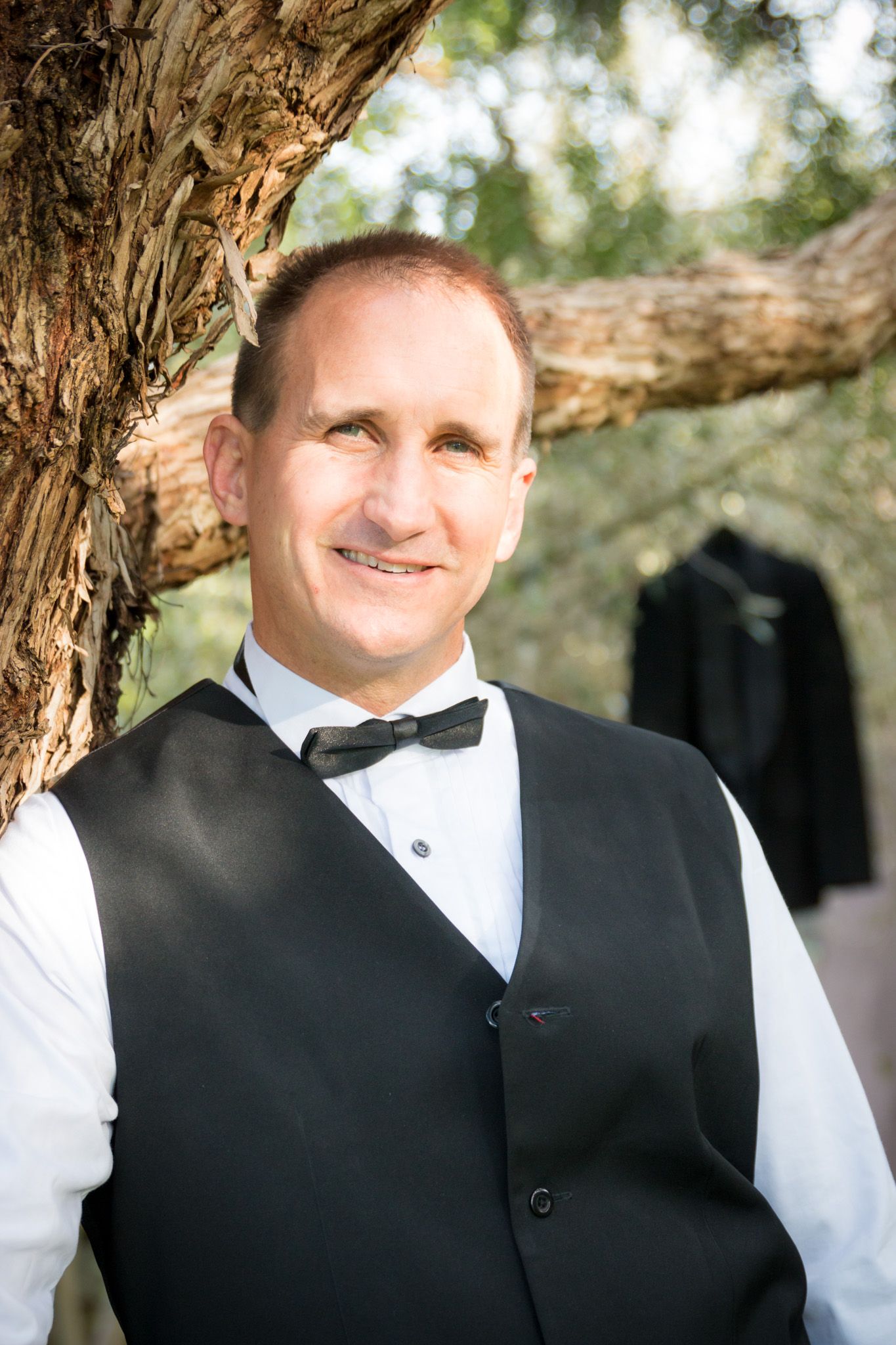 Person wearing formal black vest and white dress shirt against natural outdoor backdrop with trees.