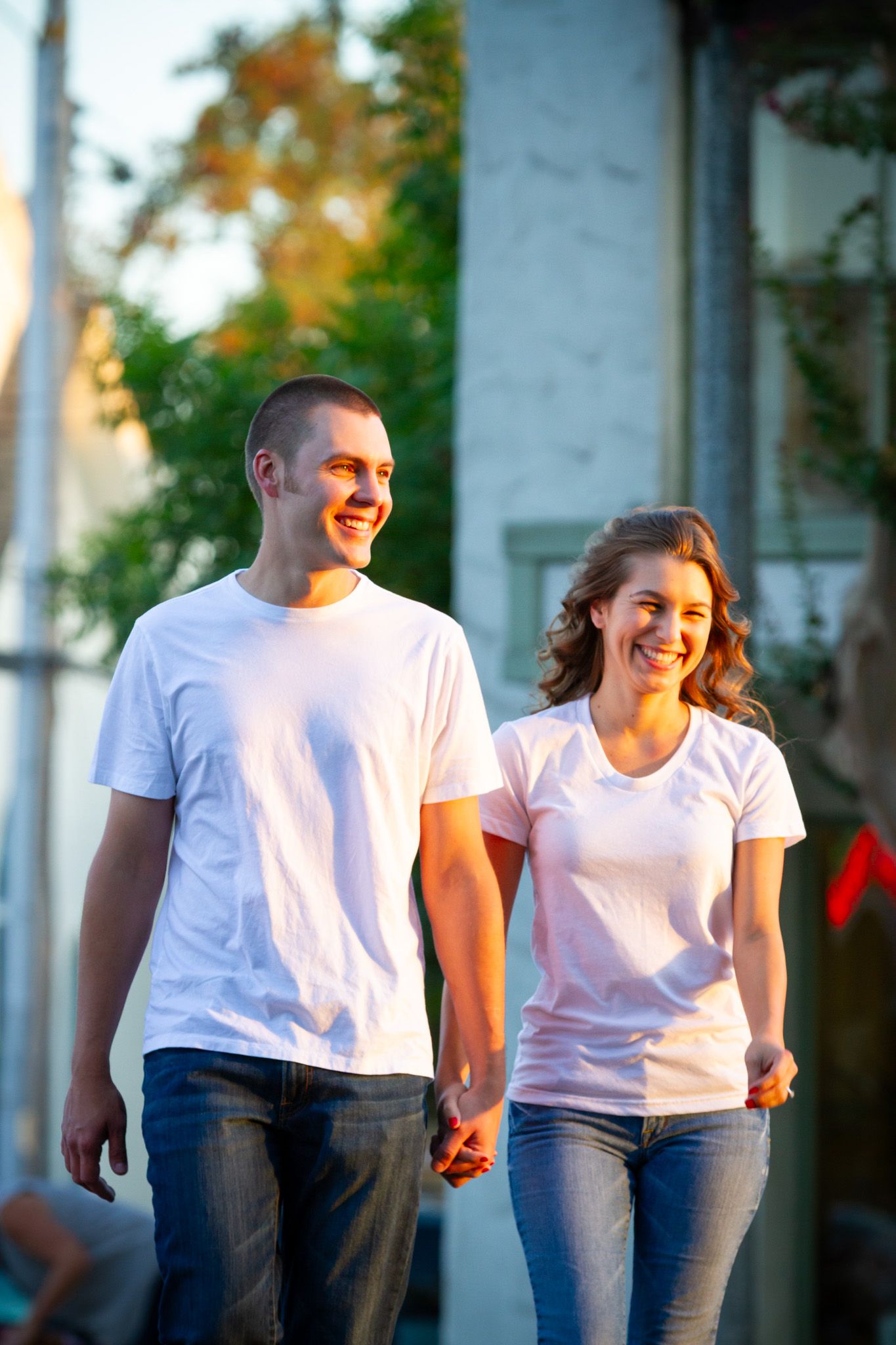 Couple in white t-shirts and jeans walking together outdoors.