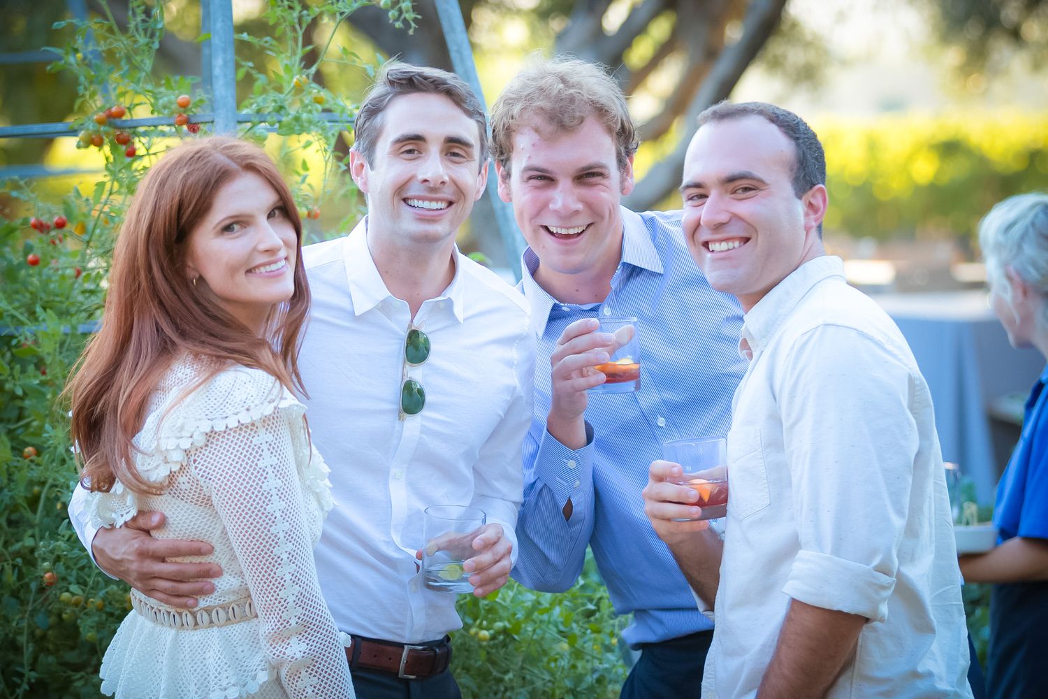 Friends enjoying drinks and smiling outdoors at a social gathering in natural lighting.
