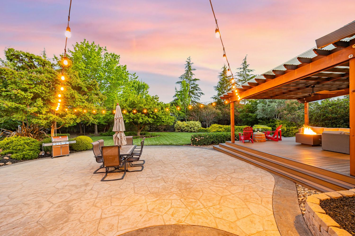 Beautiful backyard patio with string lights and rocking chairs under a pink sunset sky.