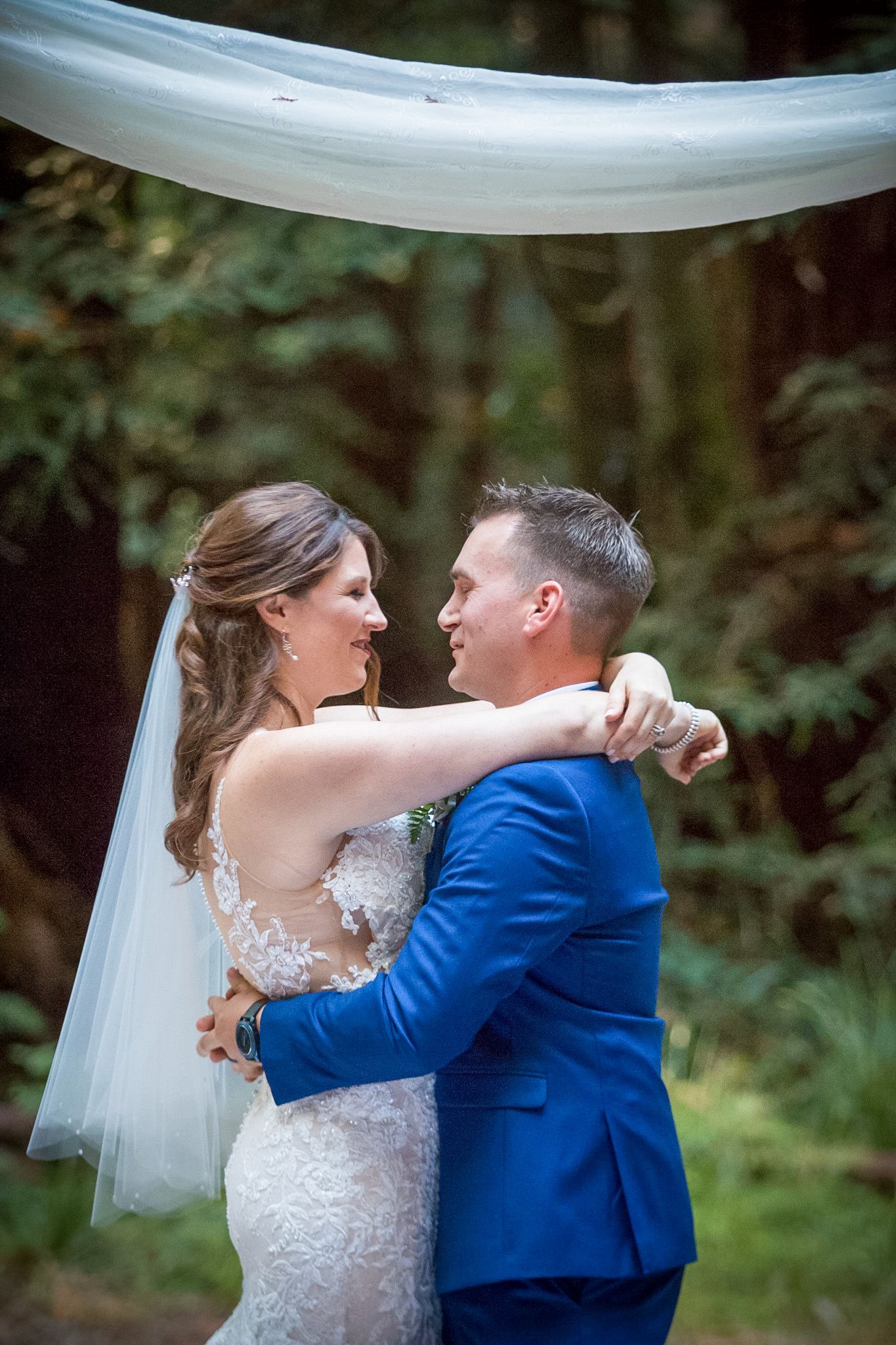 Intimate first dance moment under white fabric draping at outdoor forest wedding.