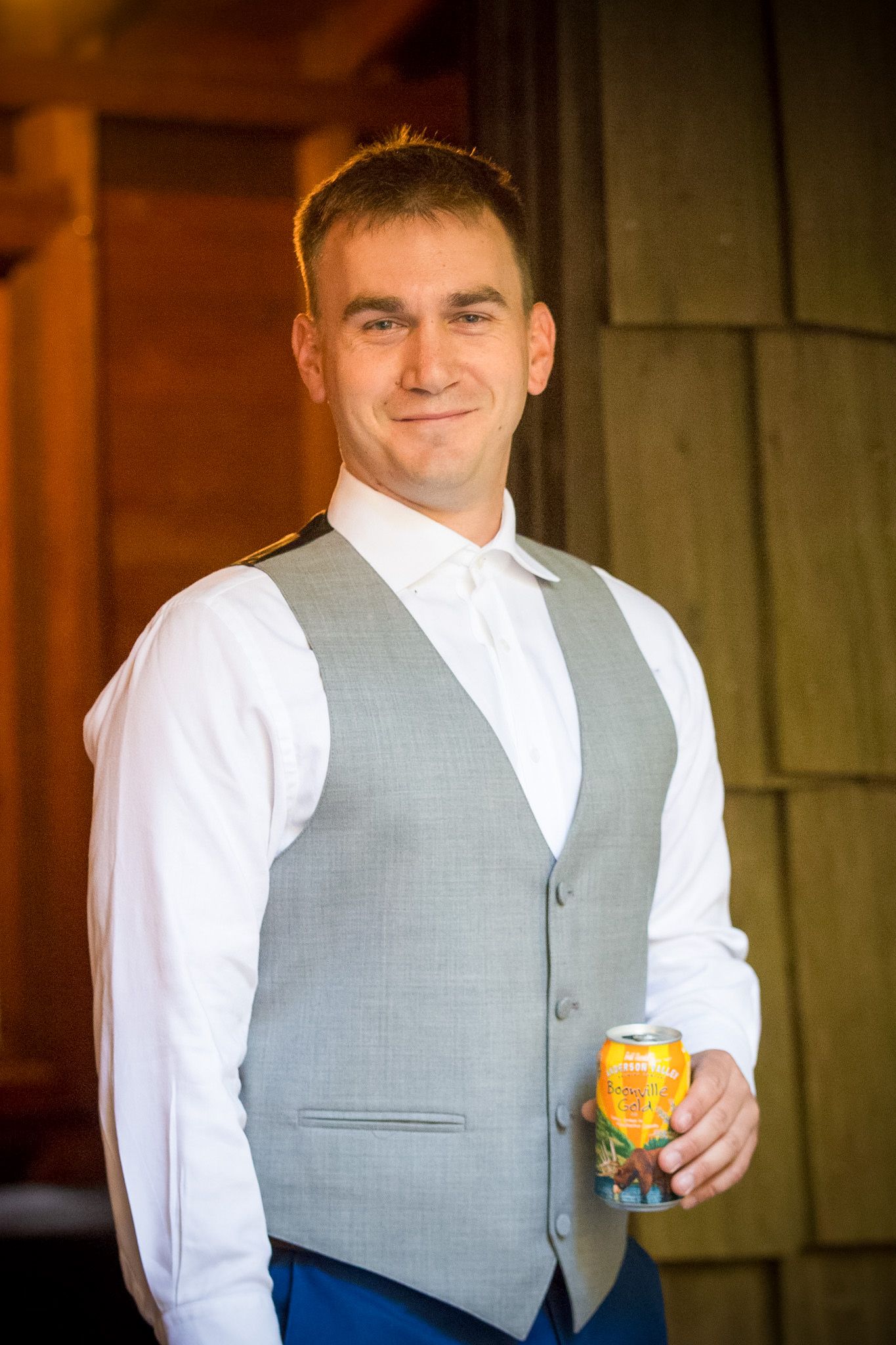 Groom in gray vest and white shirt holding beverage during wedding celebration.