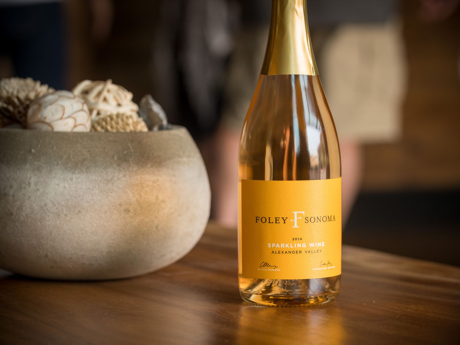 Gold champagne bottle from Valley Foothills winery next to ceramic bowl on wooden surface.