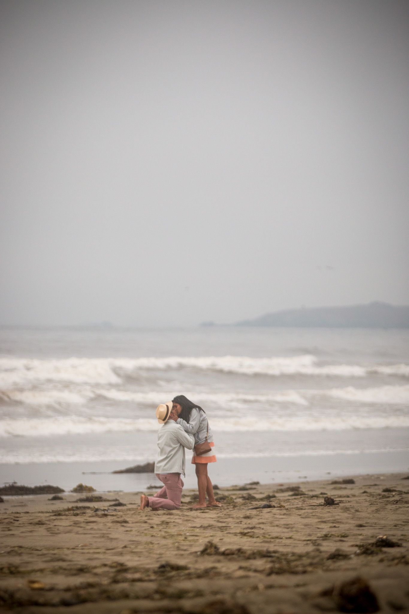 Figures standing together on sandy beach with crashing waves in background.