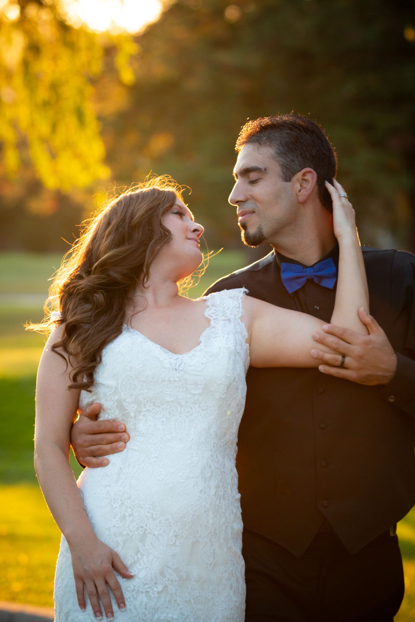 Romantic sunset portrait of newlyweds in formal attire against golden light.