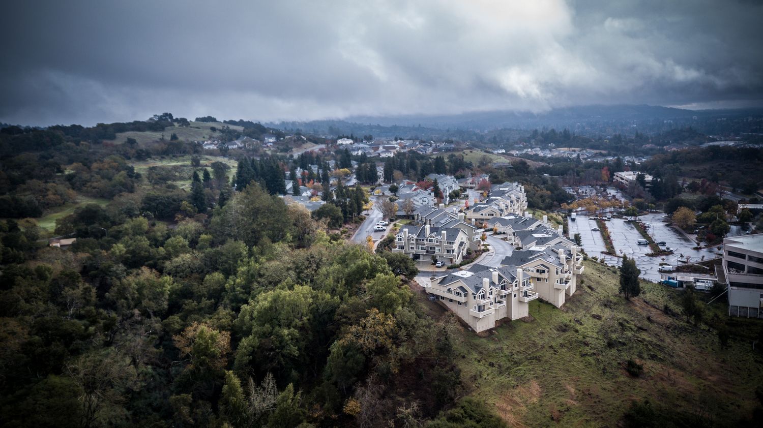 Drone view of upscale residential development with white houses nestled in green rolling hills.