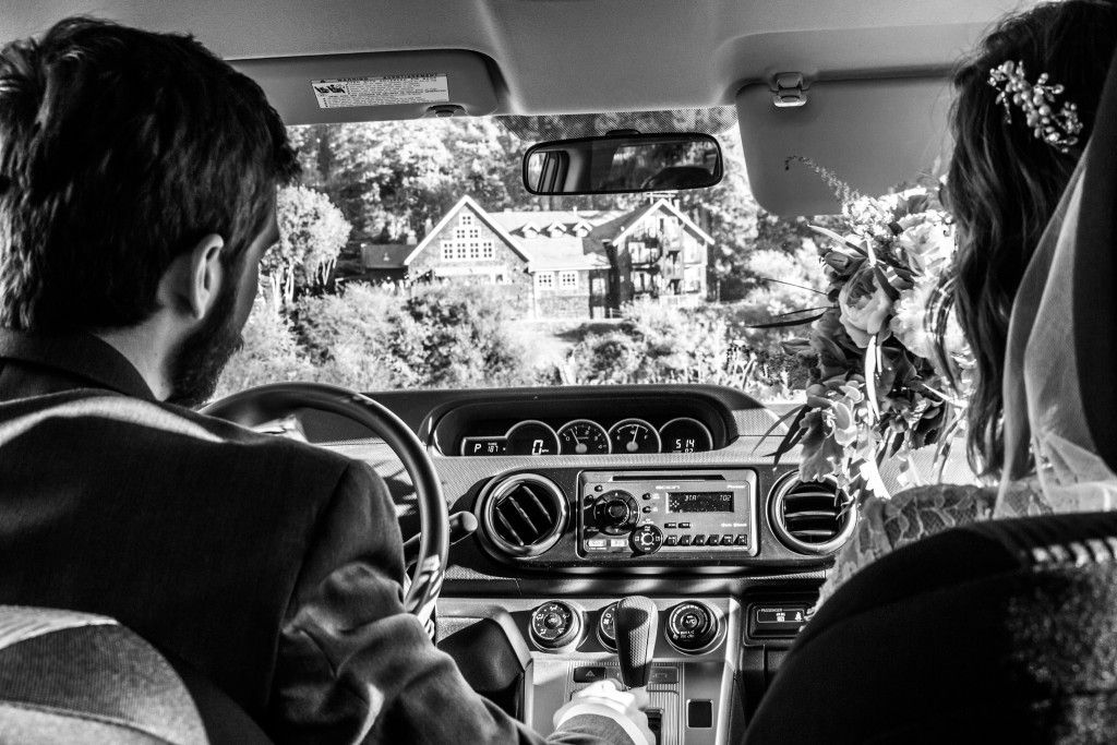 Black and white photo of a view through car windshield of countryside buildings.