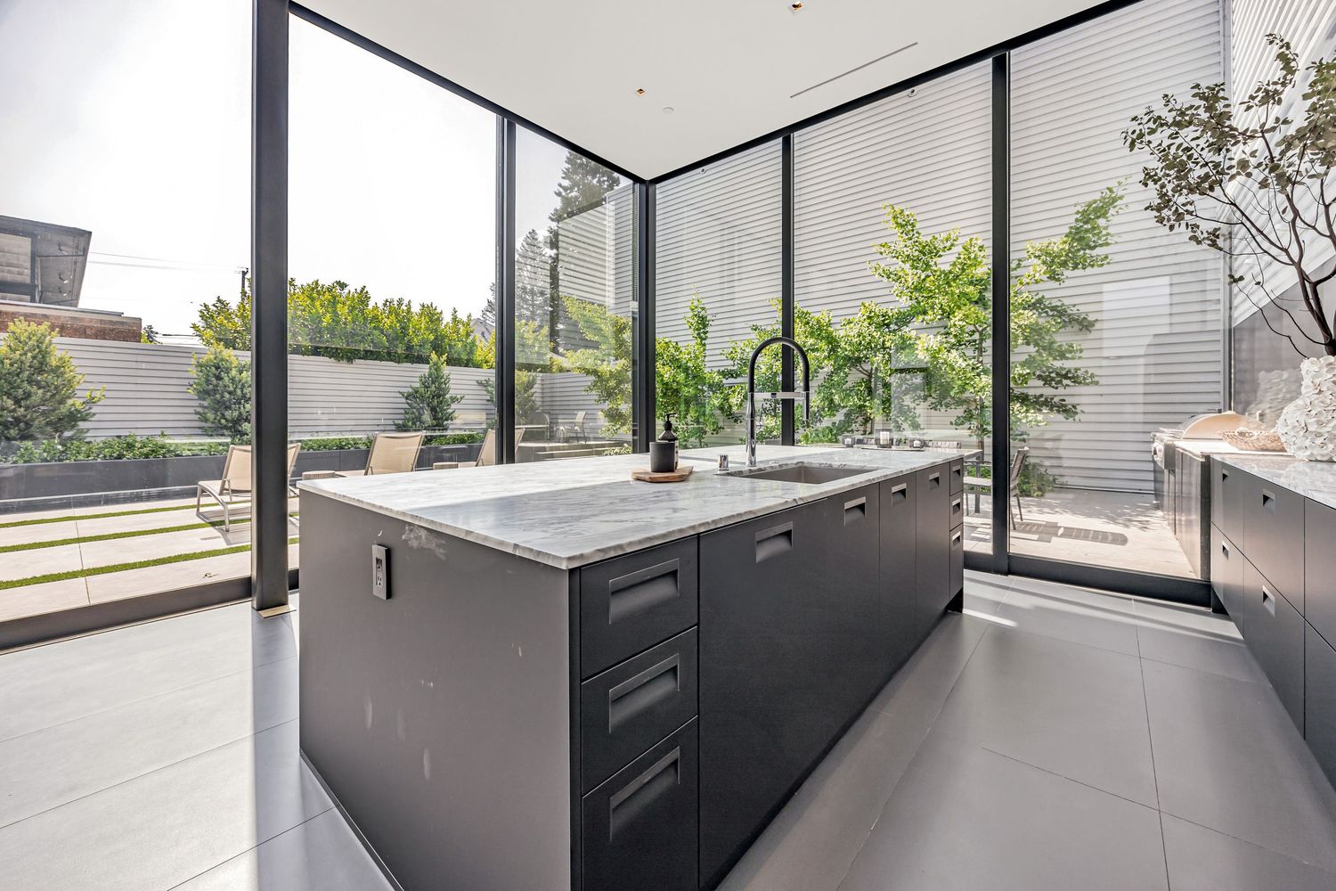 Minimalist kitchen design featuring dark cabinetry and floor-to-ceiling windows with outdoor views.
