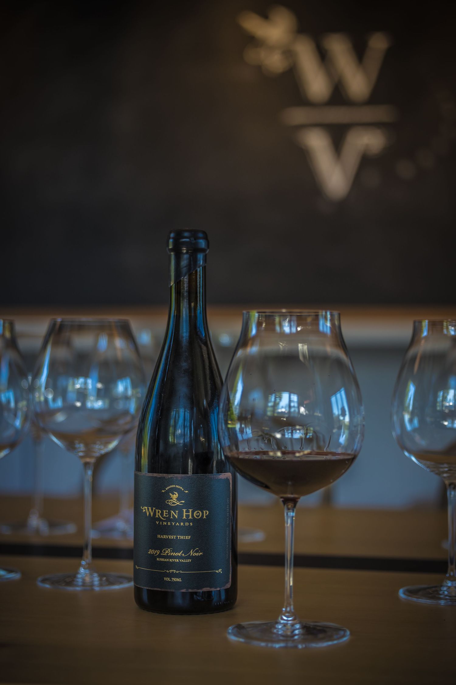 Wine bottle and glasses arranged on wooden table with moody lighting and blurred background.