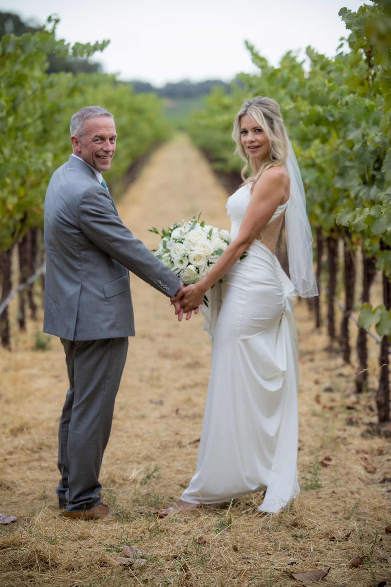 Wedding couple holding hands in vineyard row.