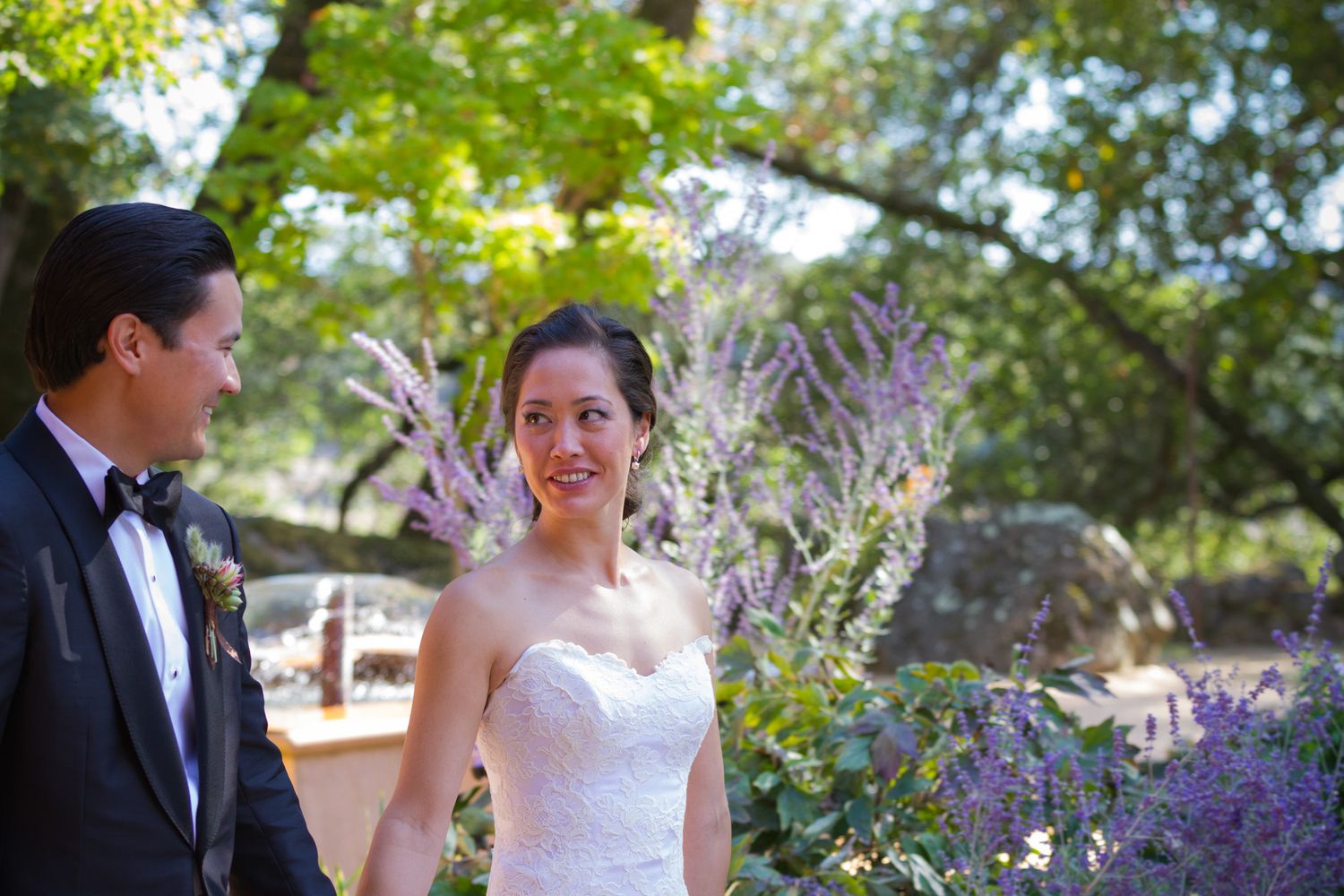 Wedding couple surrounded by blooming purple flowers in a garden setting.