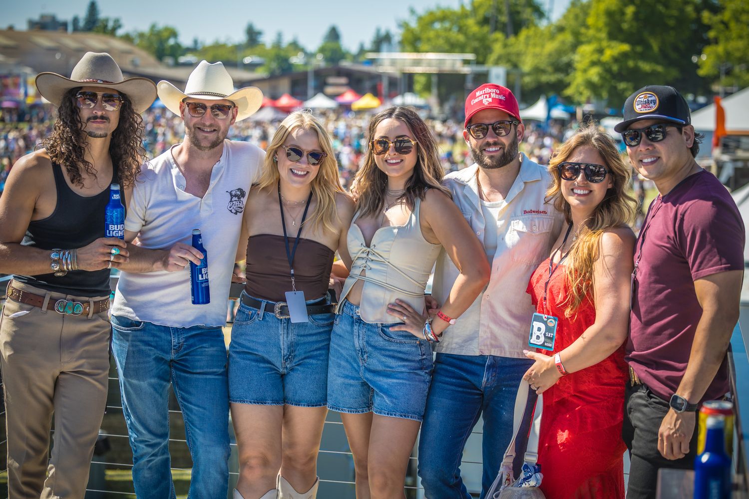 Festival goers stand together smiling and enjoying themselves at an outdoor summer music event.