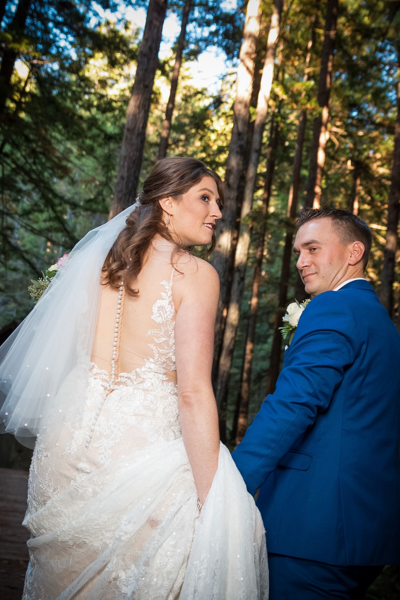 A romantic moment captured between newlyweds on a wooden bridge surrounded by tall forest trees.
