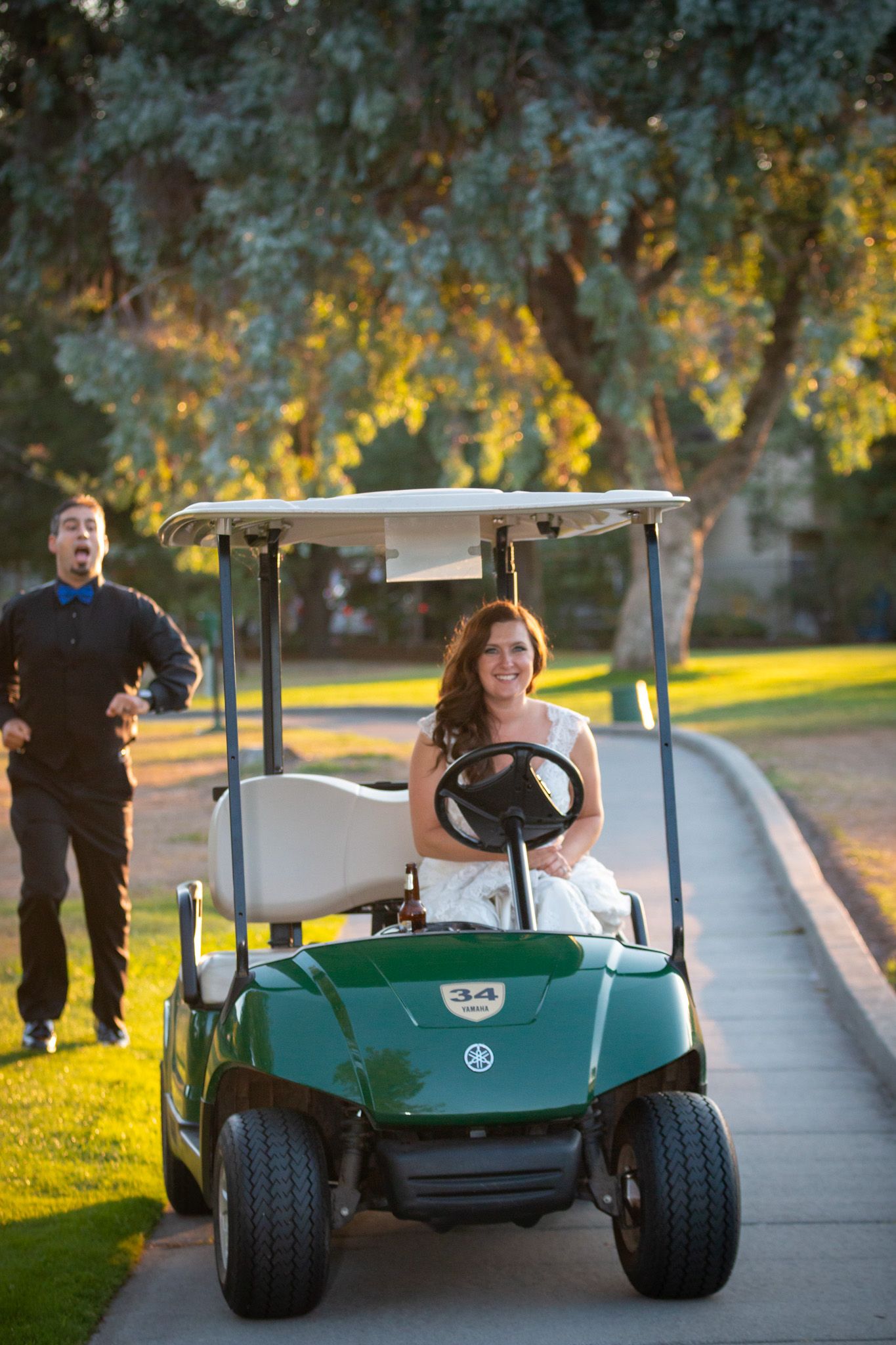 Wedding couple in a green golf cart on a path during golden hour.