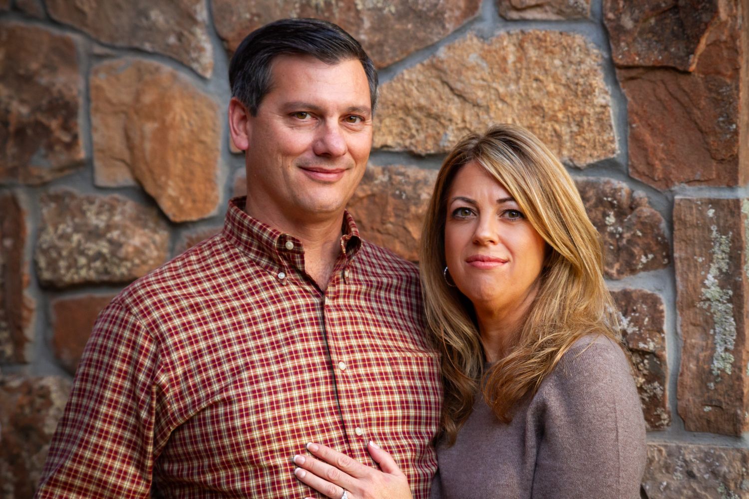 Romantic couple portraits against weathered stone wall in casual autumn attire.