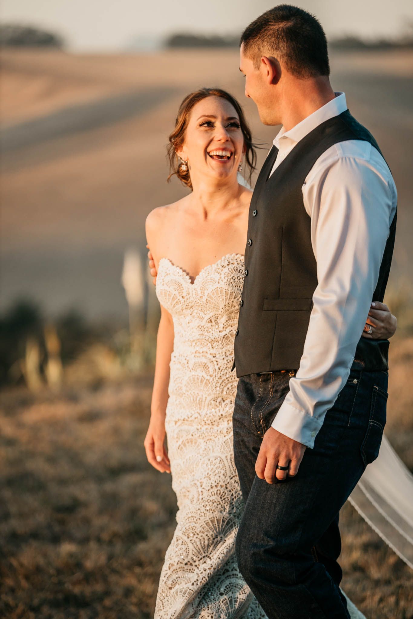 A joyful candid moment between newlyweds at sunset with rolling hills in the background.