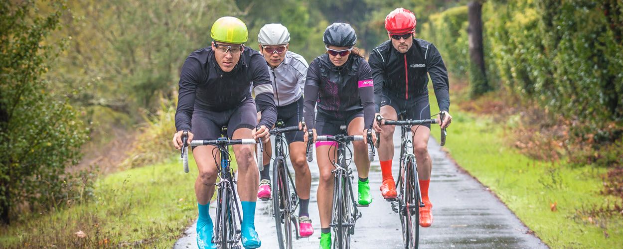 Group of cyclists riding in formation on wet country road.