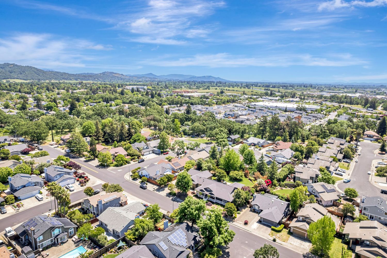 Aerial panorama of a residential neighborhood with mountain views and lush greenery.