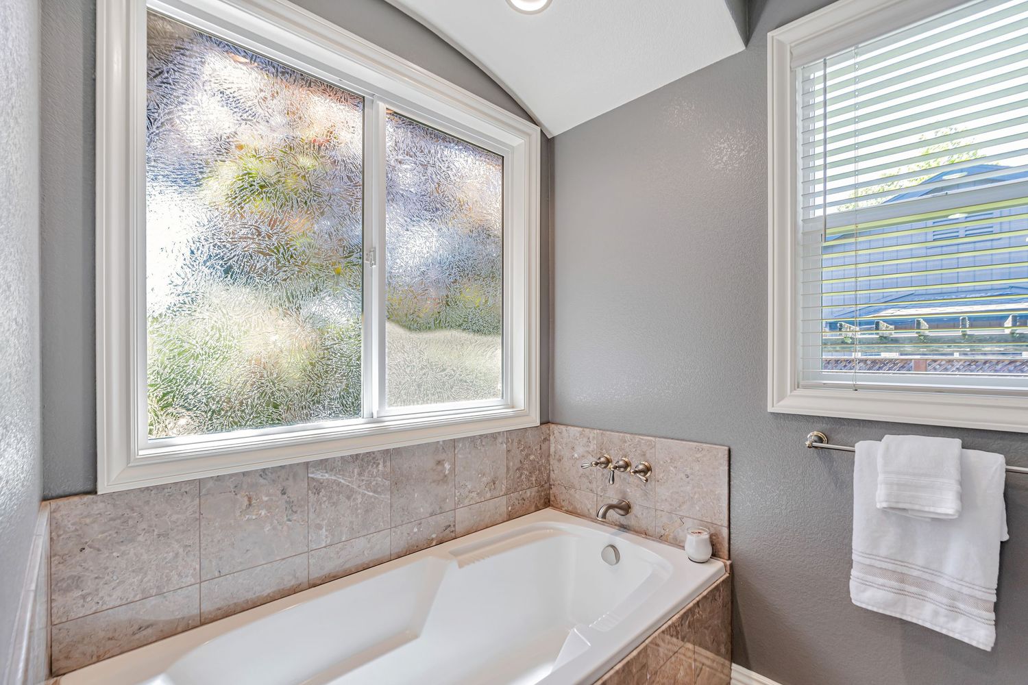 Luxurious bathroom featuring large soaking tub under window with frosted privacy glass.