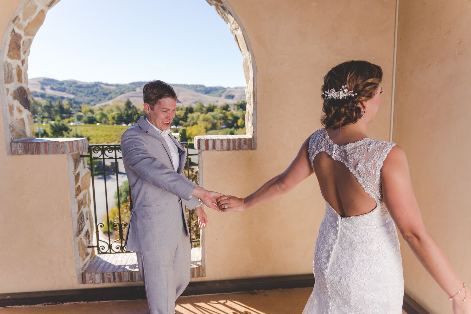 A couple stands beneath an arched entryway overlooking rolling hills during their wedding celebration.