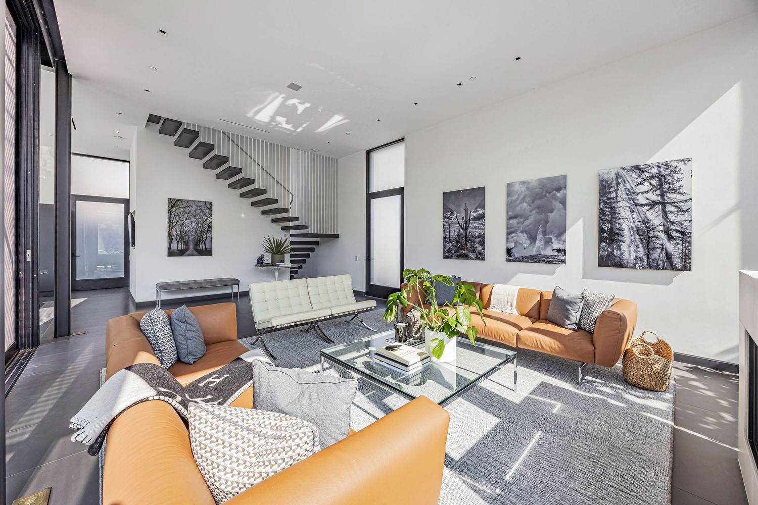 Contemporary living space featuring tan leather sofas, black and white artwork, and a floating staircase.