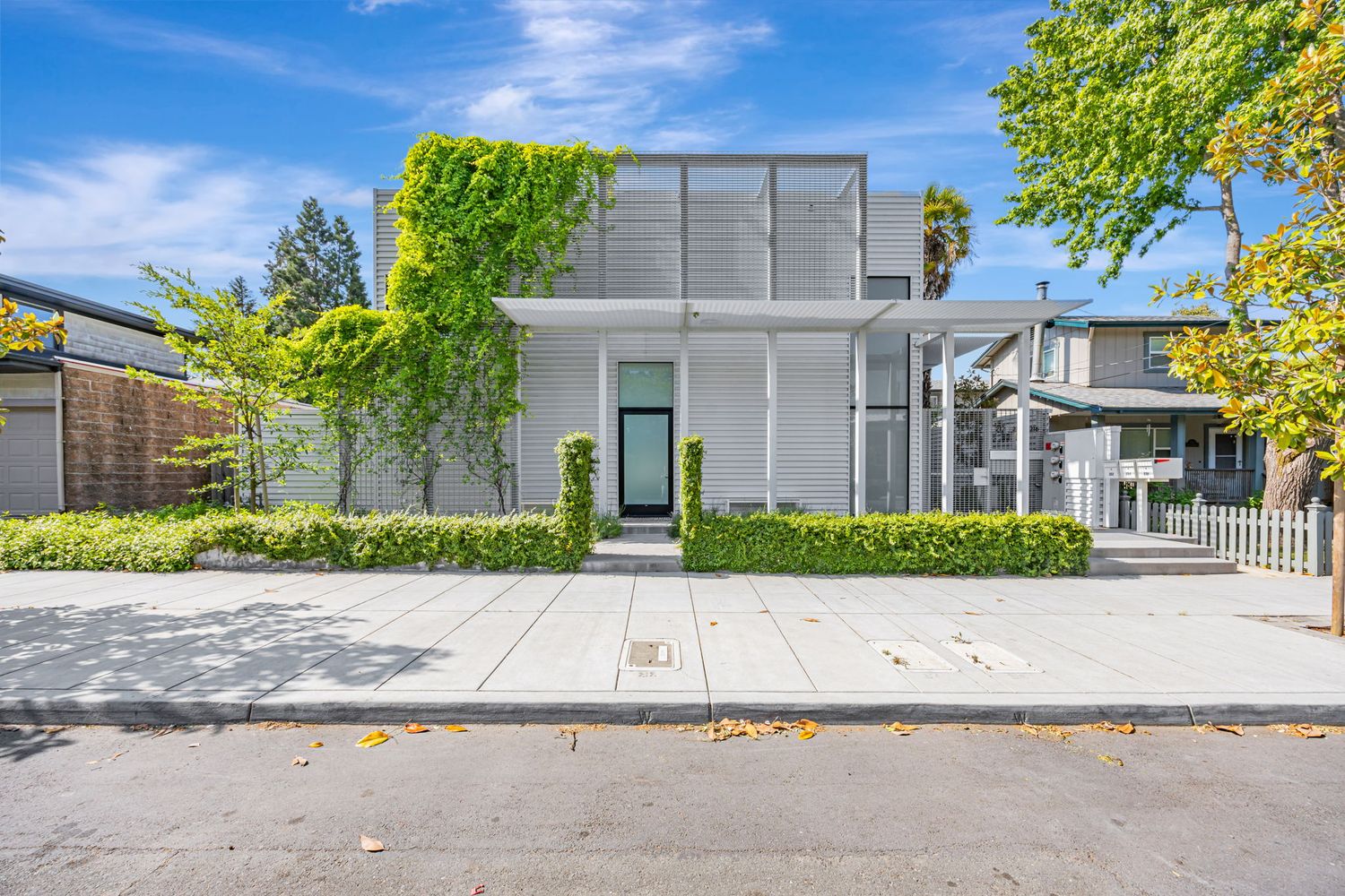 Modern white minimalist house exterior with large windows and lush landscaping.