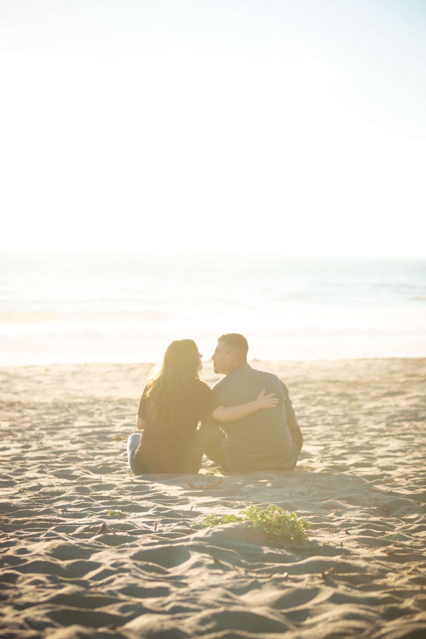 Silhouetted couple sitting close together on sandy beach at sunset.