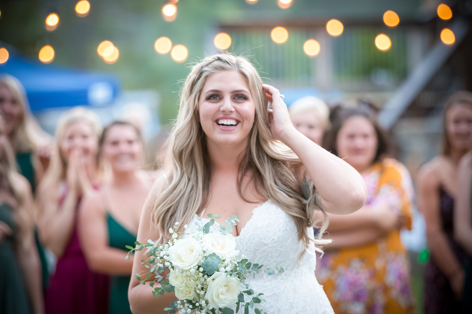 A bride holds her bouquet while celebrating with guests under string lights at an outdoor reception.