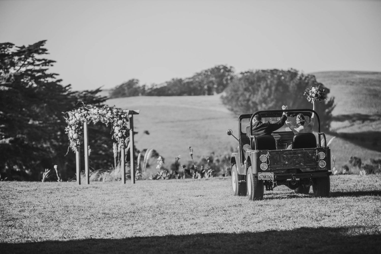 A black and white photo of a vintage truck arriving at an outdoor wedding ceremony site.