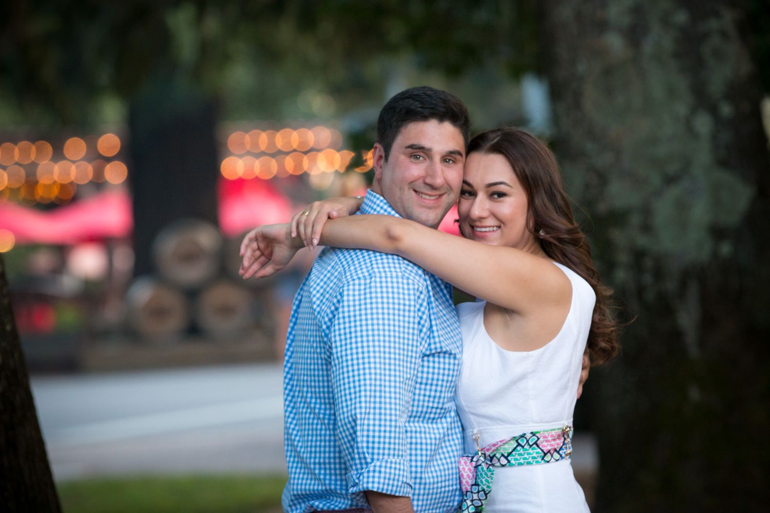 A happy couple embraces outdoors at dusk with blurred lights in the background.