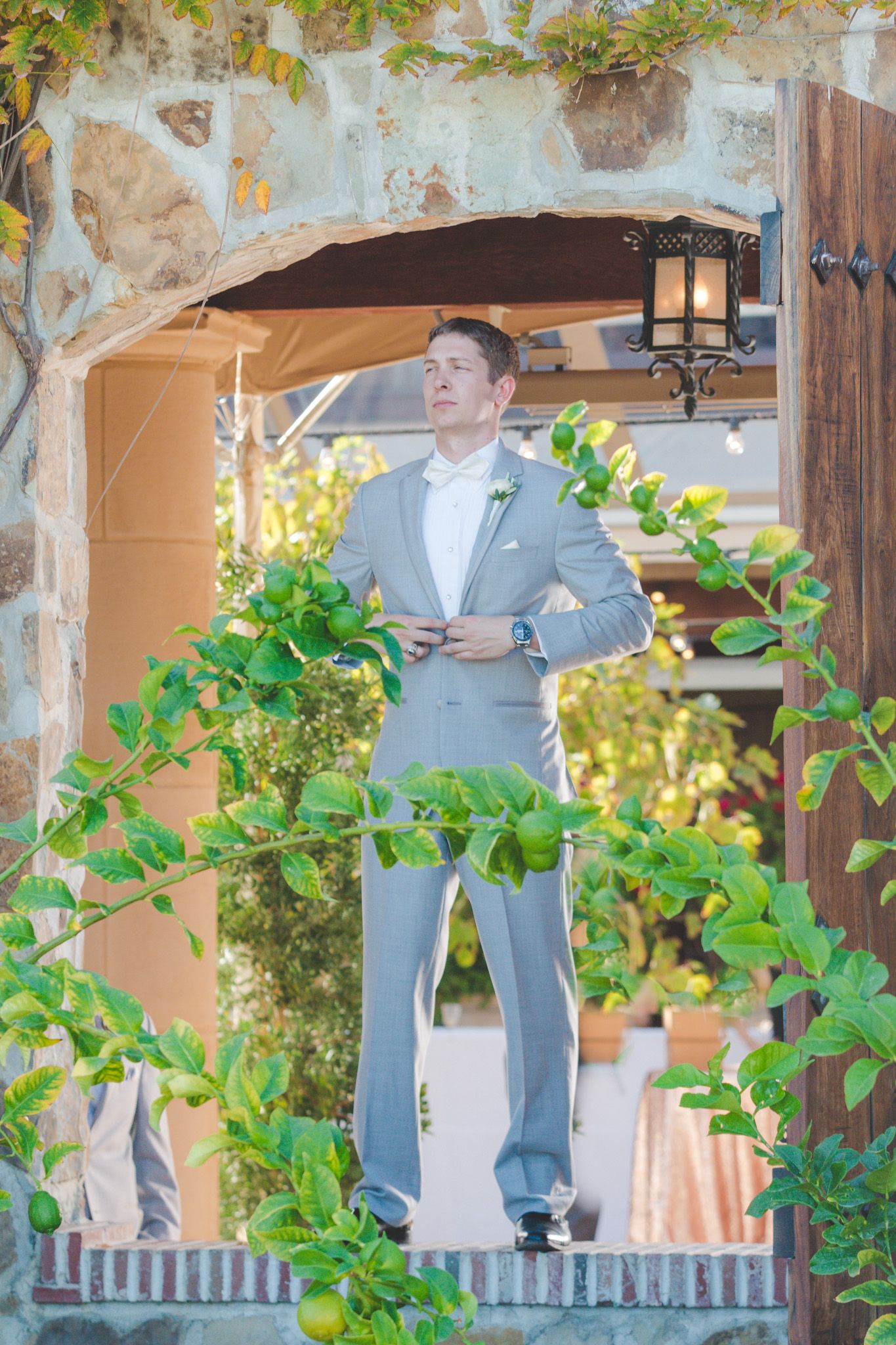 Light gray suited figure standing in an arched doorway with green vines and natural light.