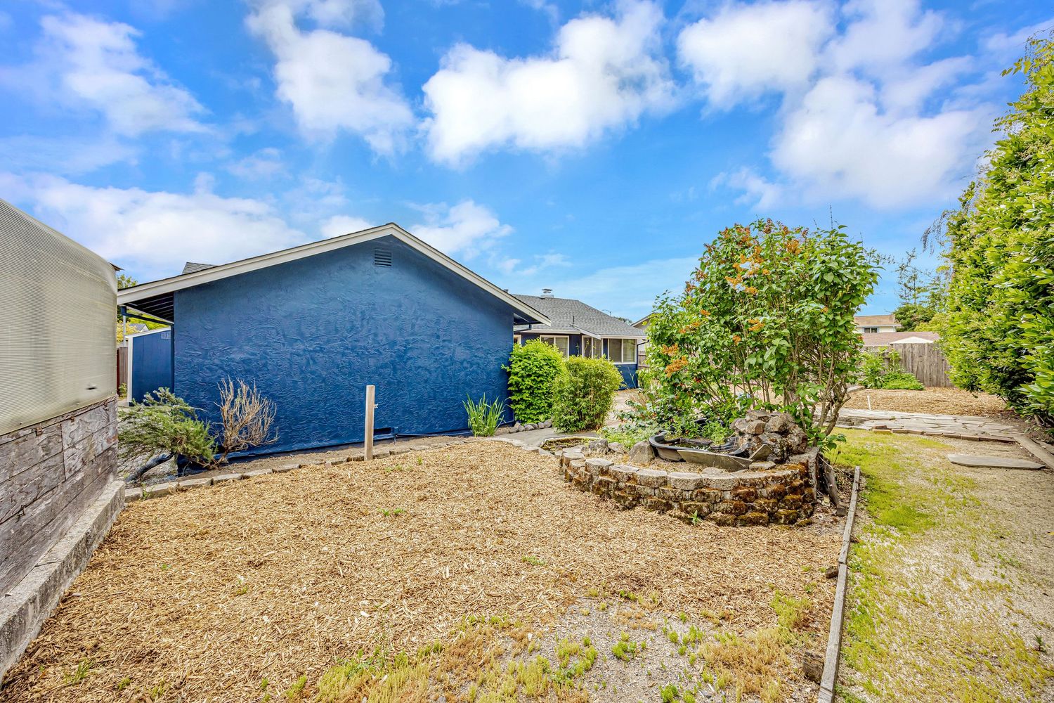 Rear view of blue house with raised garden bed and gravel landscaping.