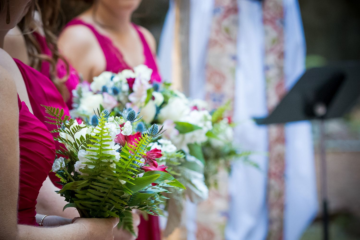 Bridesmaid holding elegant bouquet featuring ferns and flowers in bright magenta dress.