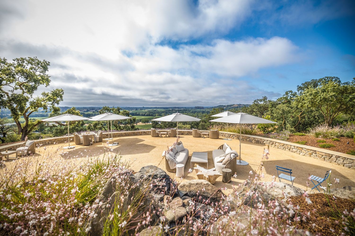 Scenic outdoor lounge area with comfortable chairs overlooking a coastal landscape under blue skies.