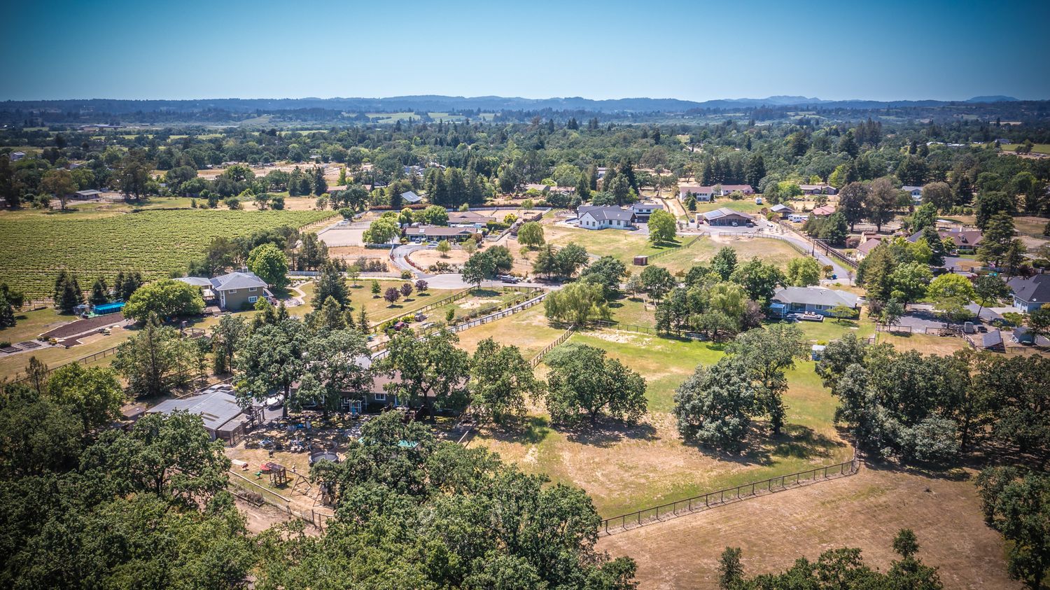 Aerial view of a suburban neighborhood with scattered houses, trees, and open spaces under blue sky.
