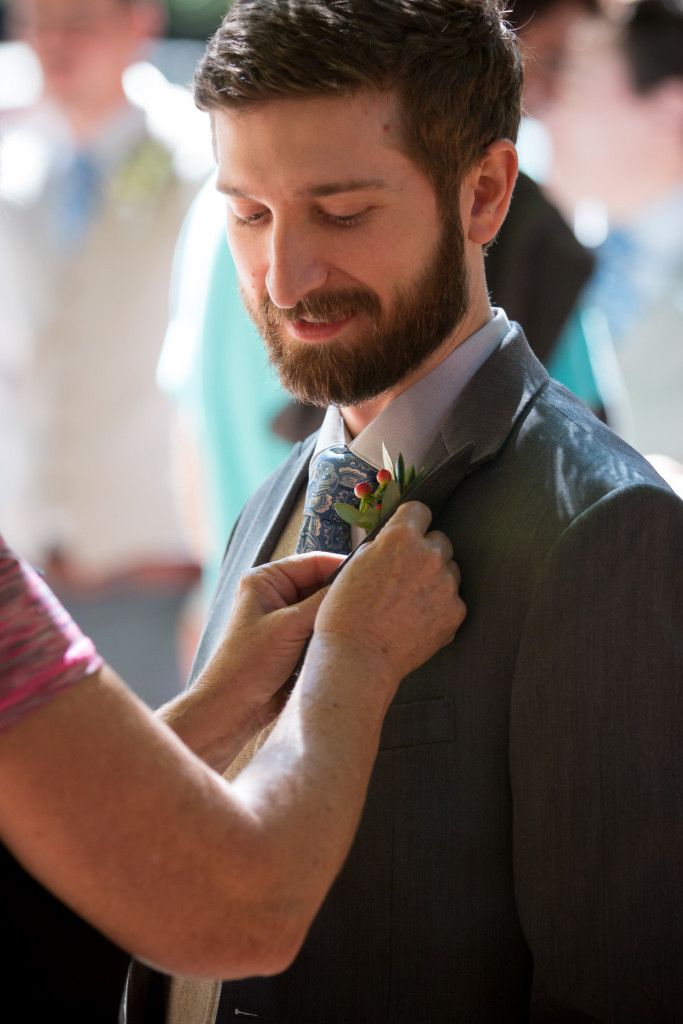 Close-up of a boutonniere being pinned on a grey suit at a formal event.